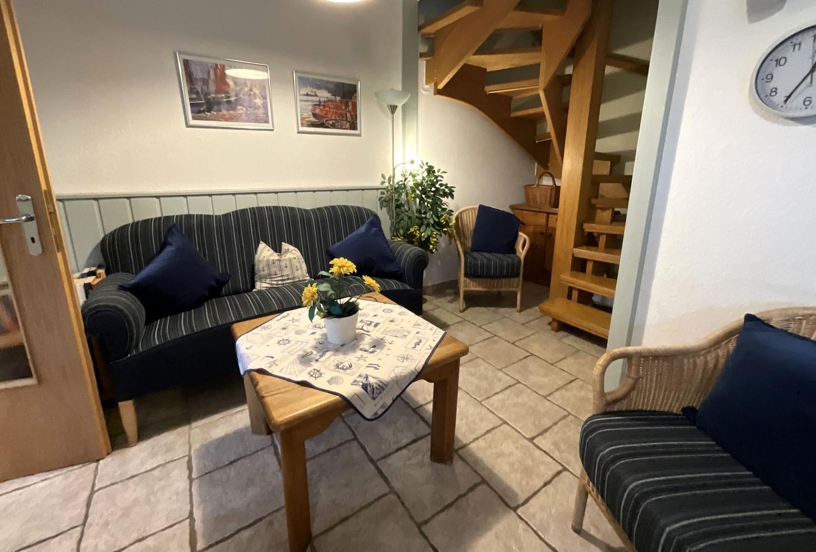 Wohnzimmer mit Sofa, Sessel und Holztreppe.