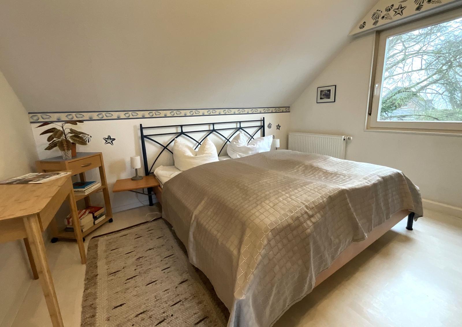 Schlafzimmer mit Dachschrägen, Bett, Nachttisch und Fenster.