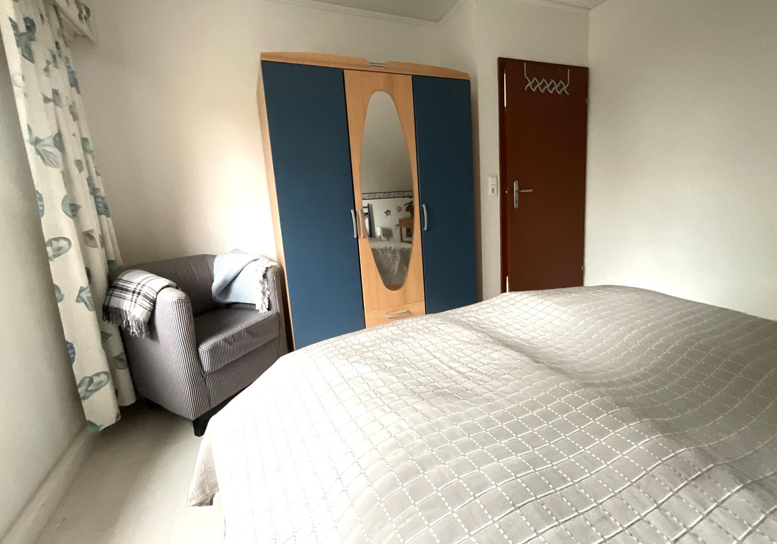 Schlafzimmer mit Bett, Kleiderschrank und Sessel.