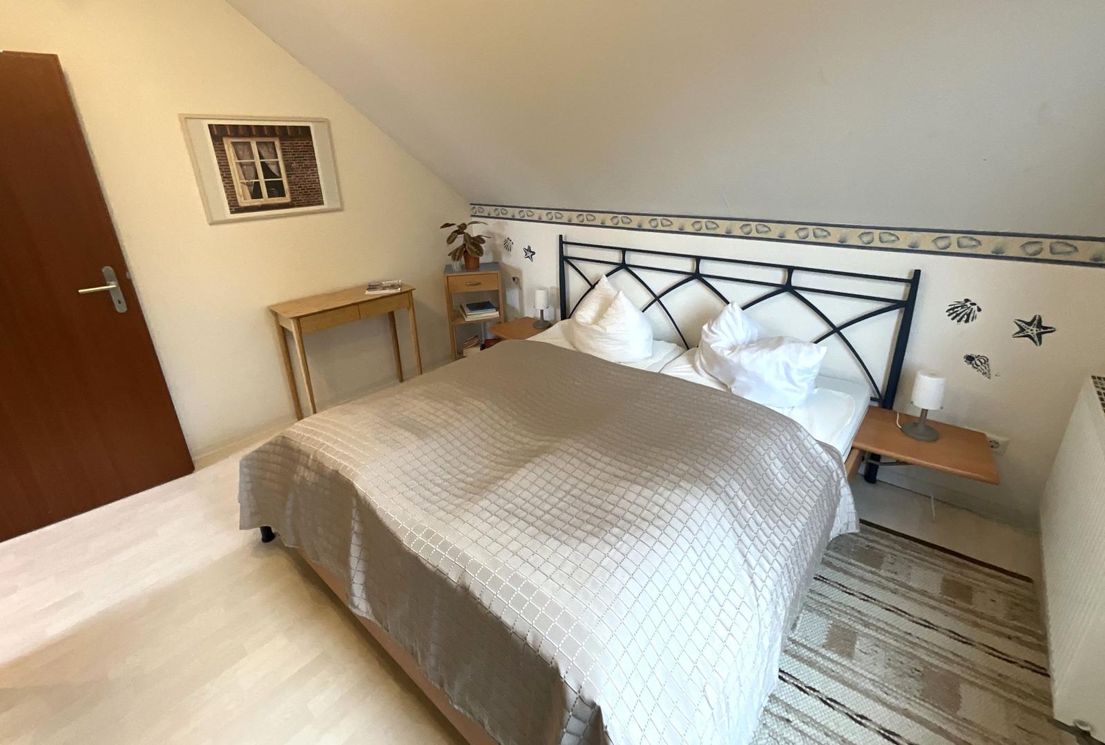 Schlafzimmer mit Dachschrägen, Bett, Nachttischen und Schreibtisch.