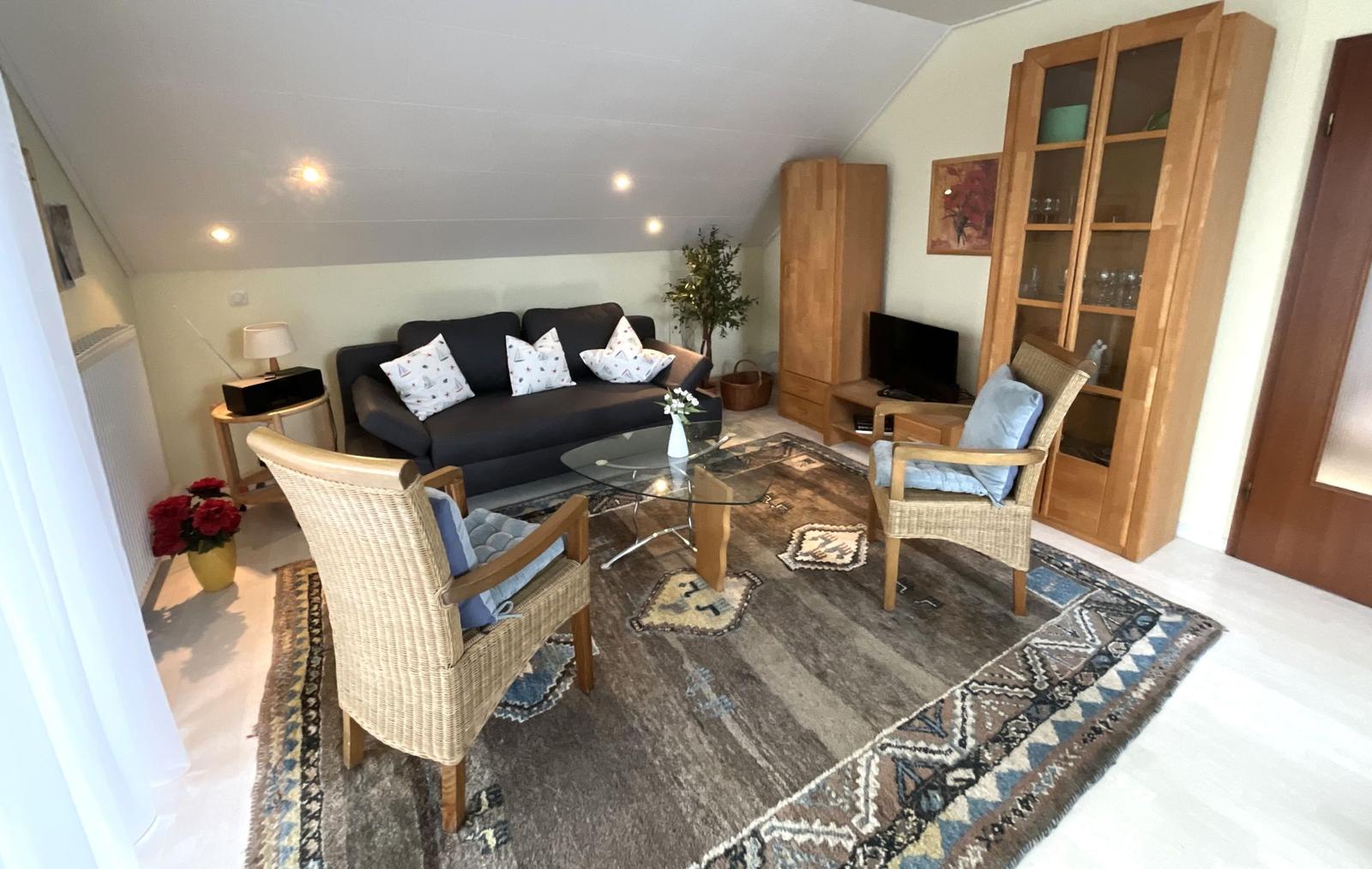 Wohnzimmer mit Sofa, zwei Sesseln und Glas-Tisch auf Teppich.