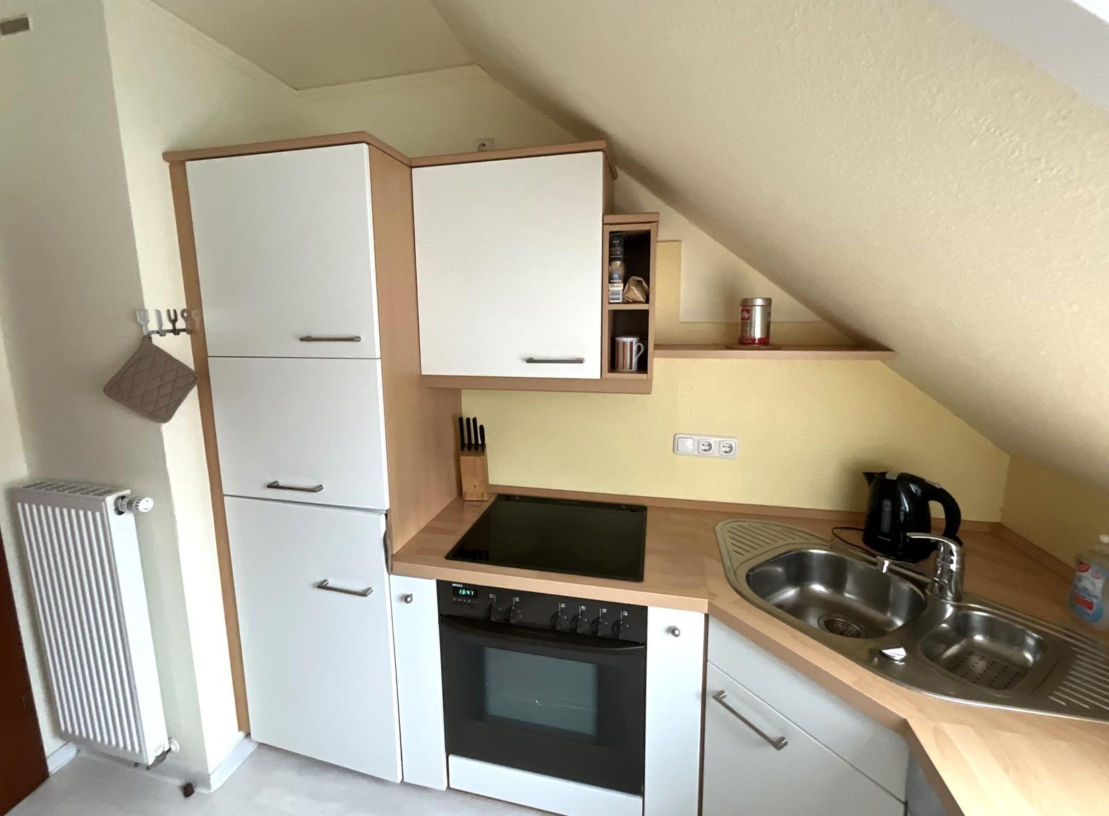 Küche mit Kochfeld, Herd, Spüle und Schränken unter schräger Decke.
