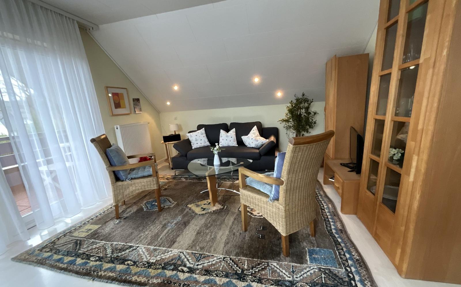 Wohnzimmer mit Sofa, zwei Sesseln und Glas-Tisch auf Teppich