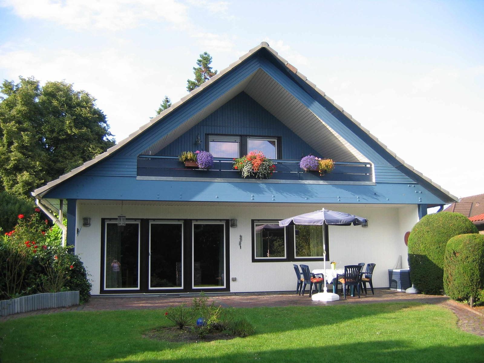 Ein Haus mit blauem Dach und Balkon, Gartenbereich mit Tisch und Sonnenschirm.