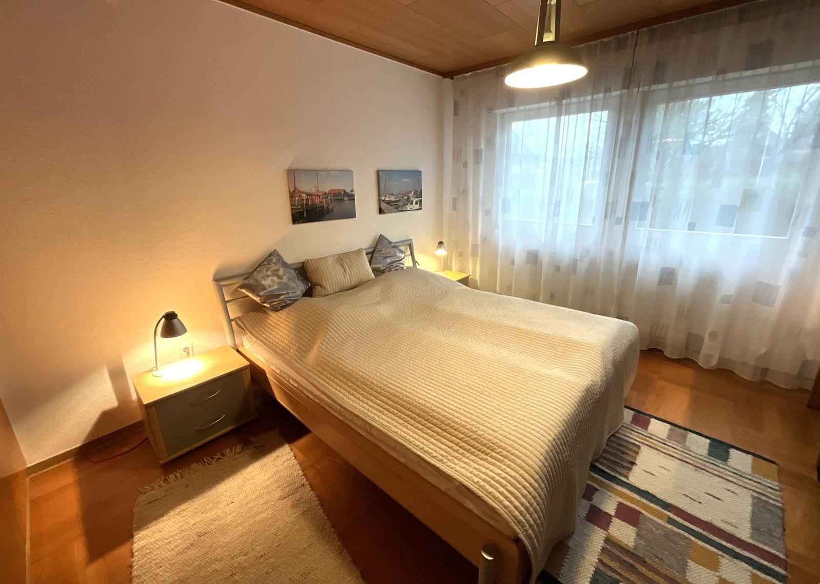 Schlafzimmer mit Bett, Nachttisch und Fenster mit Vorhängen.