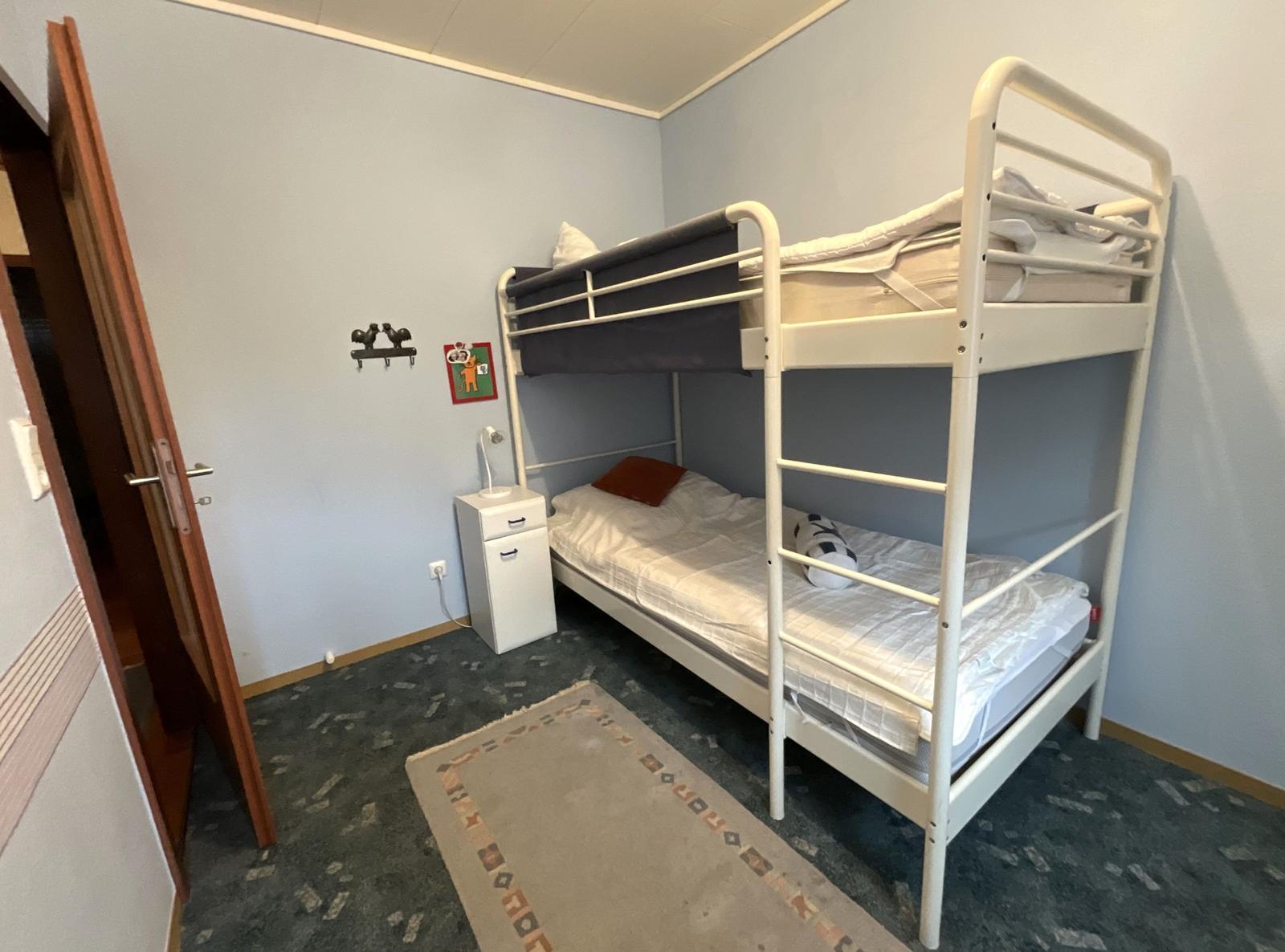 Zimmer mit Doppelstockbett, Nachttisch und Teppich auf Teppichboden.