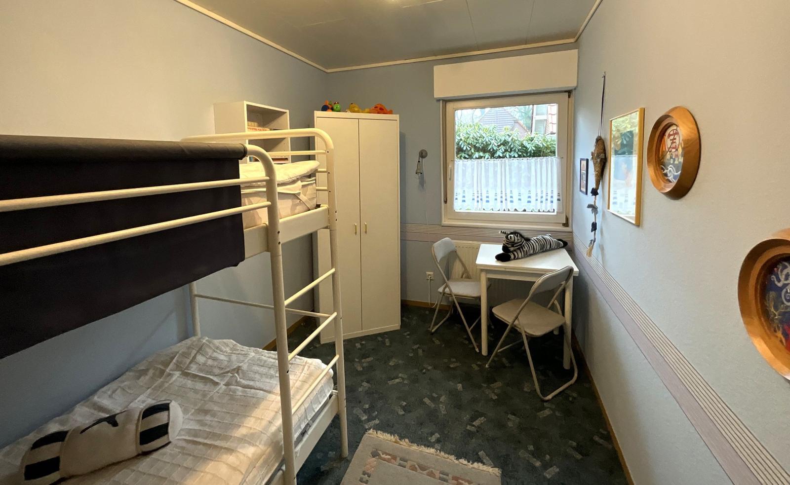 Zimmer mit Doppelstockbett, Schreibtisch und Fenster mit Blick auf Garten.