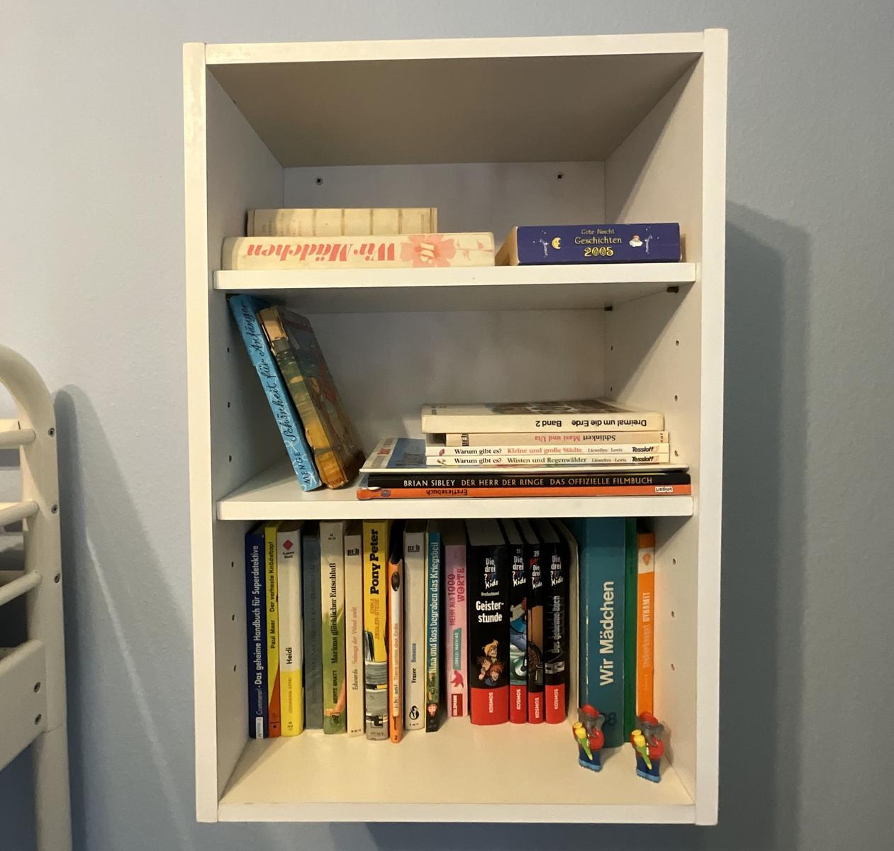 Weißer Bücherregal mit drei Etagen und Büchern sowie zwei Figuren.