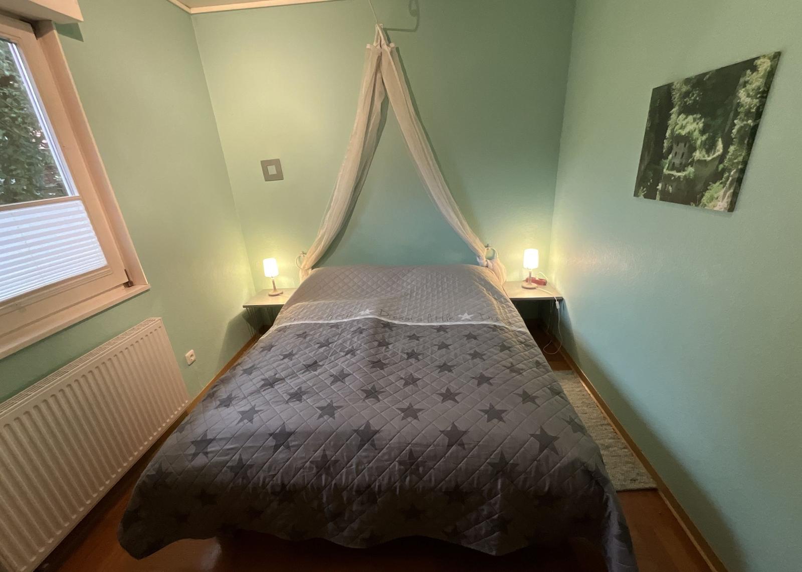 Schlafzimmer mit Bett, Baldachin, zwei Nachttischen und Wandbild.