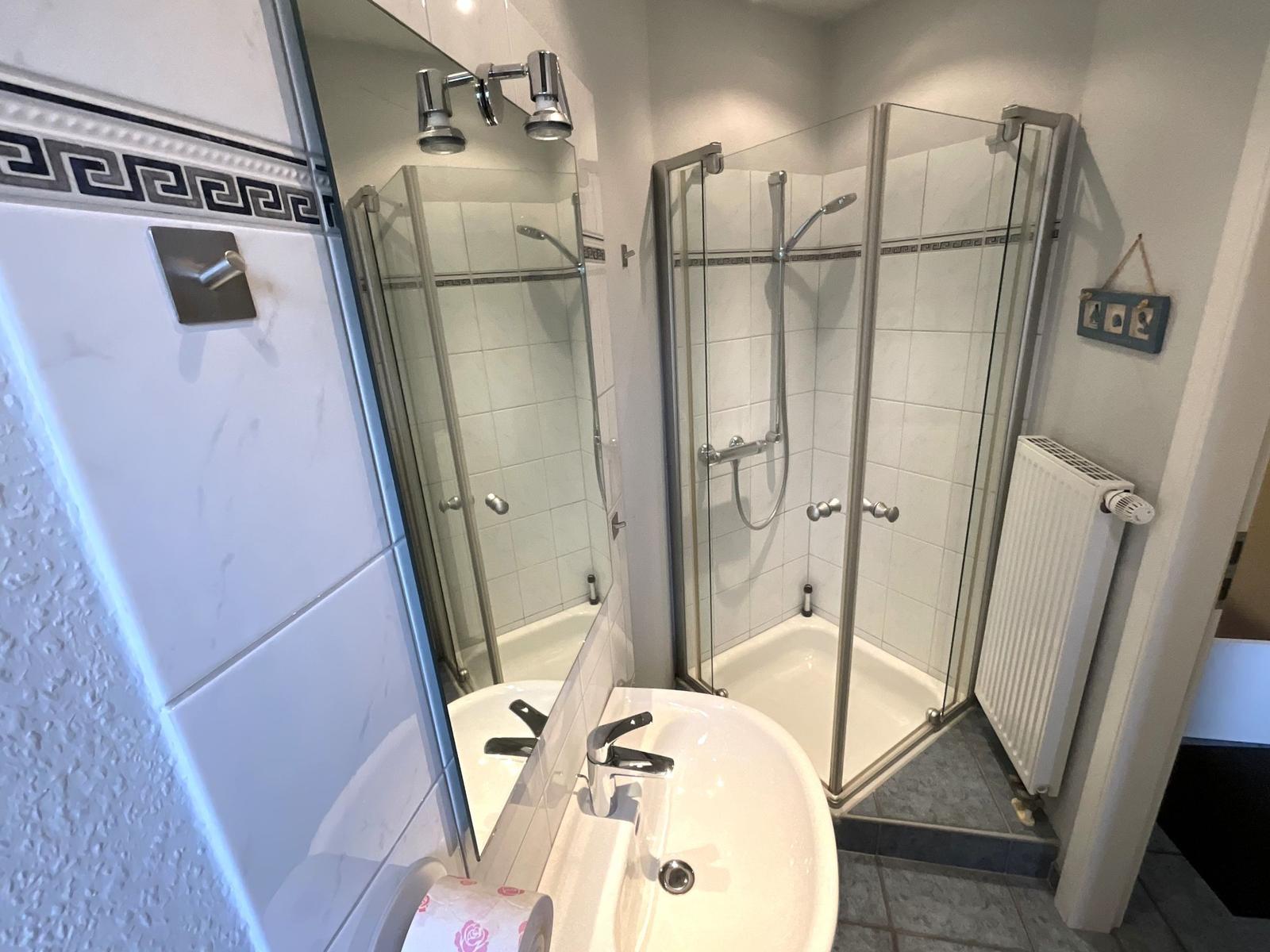 Badezimmer mit Dusche, Waschbecken und Spiegel