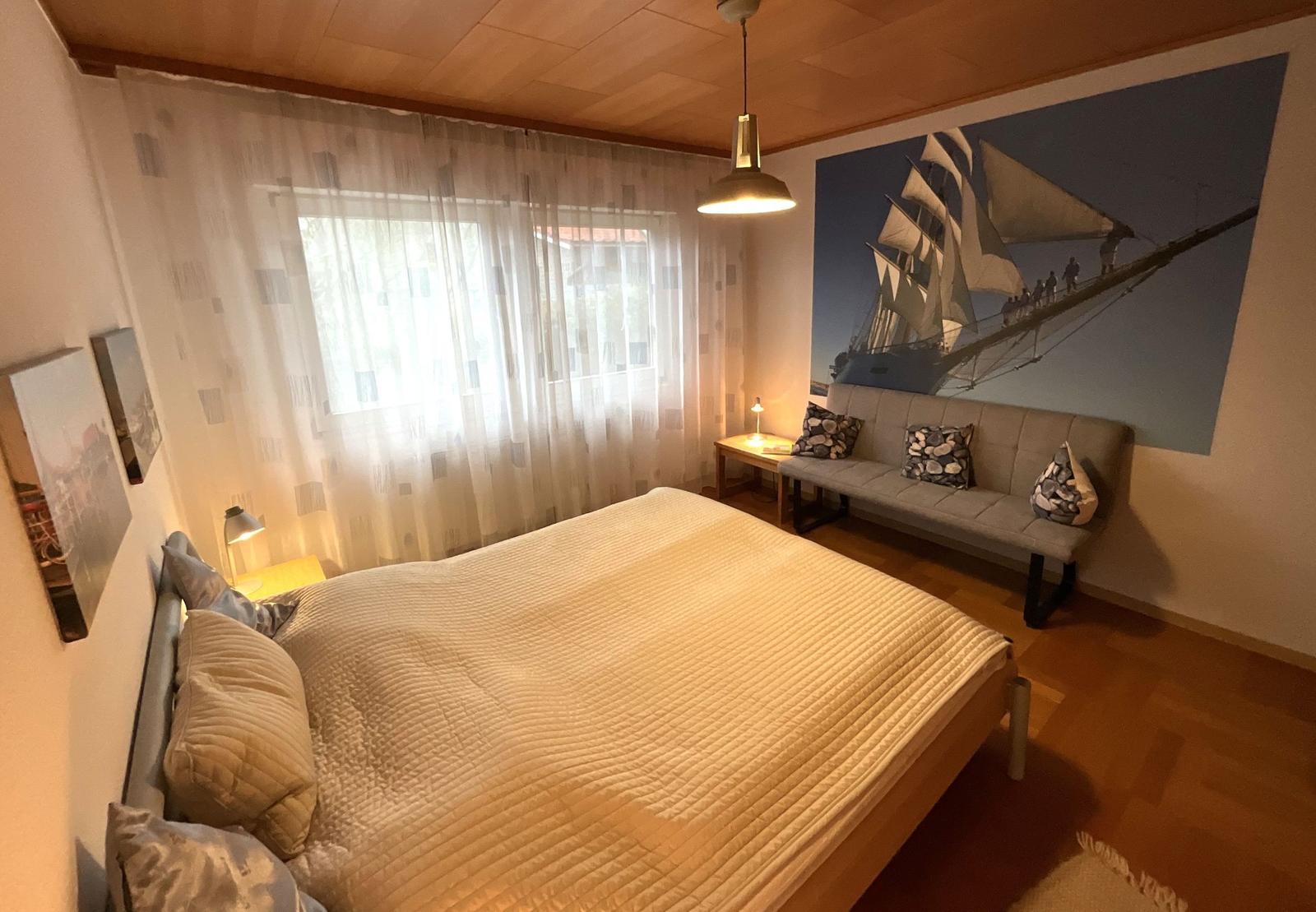 Schlafzimmer mit Bett, Sofa und Wandbild eines Segelschiffs.