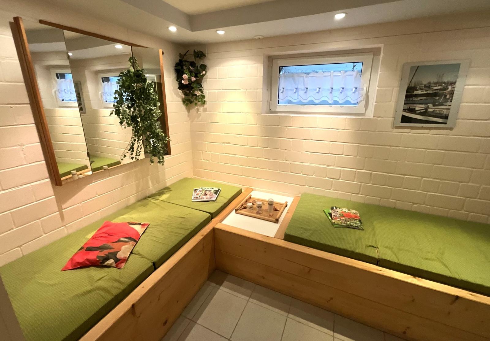 Zwei grüne Matratzen auf Holzrahmen, Wandspiegel, Pflanze, Fenster und Bild.