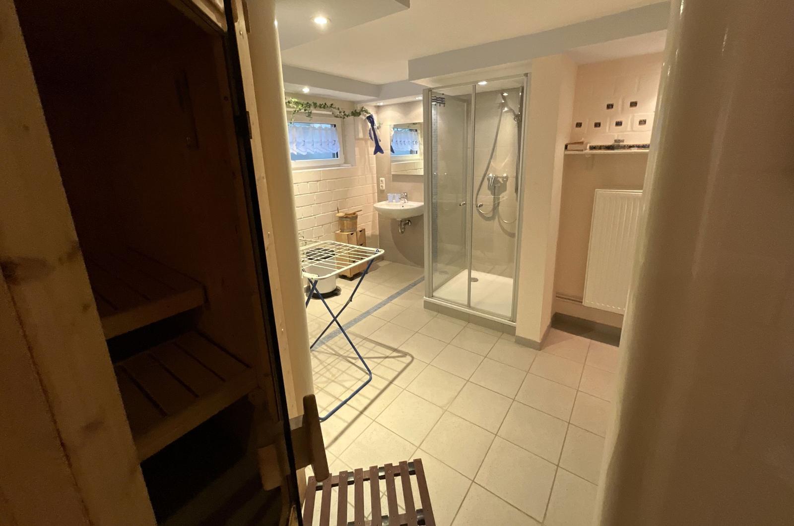 Bad mit Dusche, Waschbecken und Sauna im Hintergrund