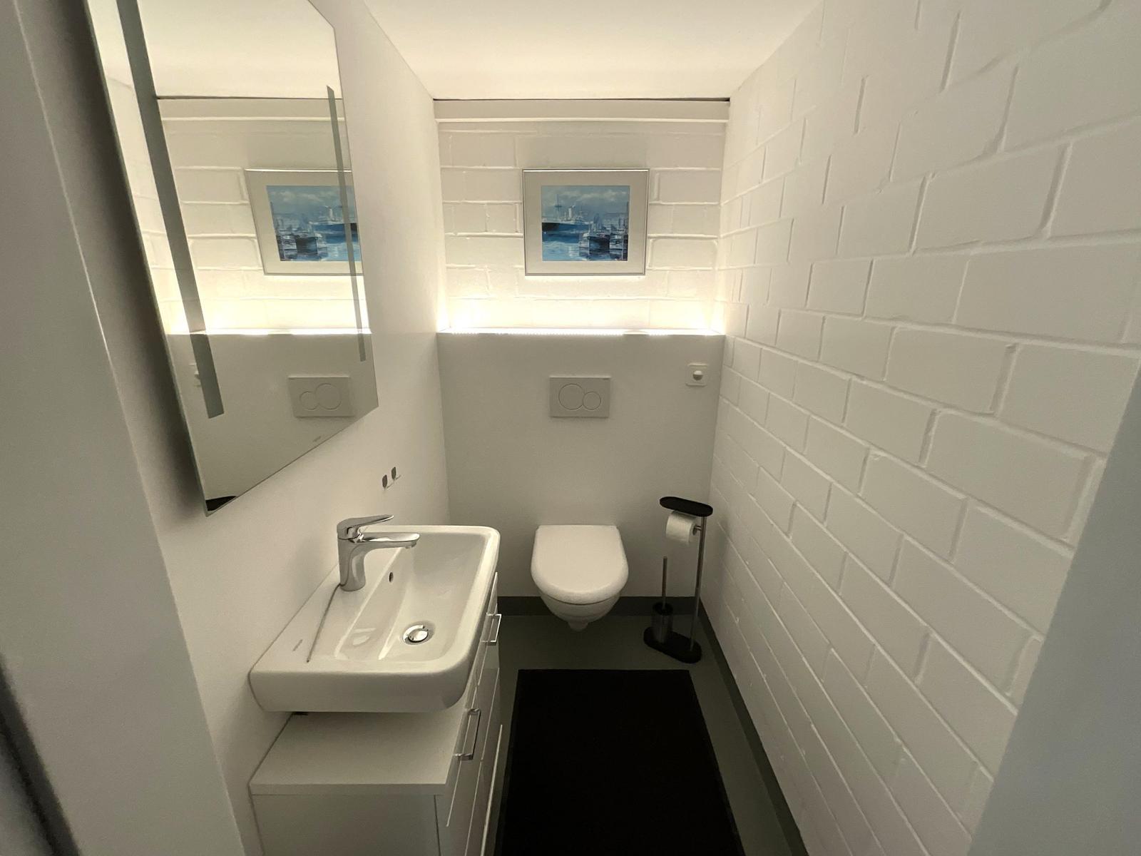 Badezimmer mit Waschbecken, Toilette und Spiegel an weißen Wänden.