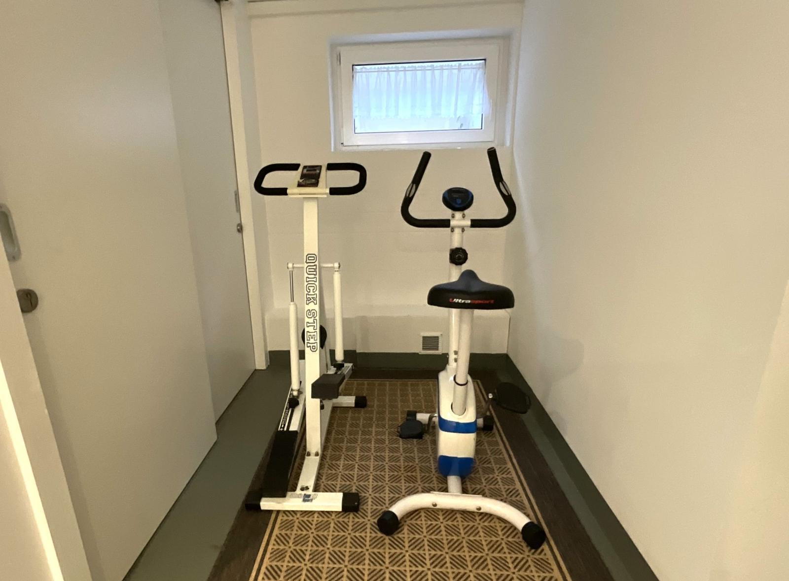 Fitnessraum mit Stepper und Fahrradtrainer unter einem Fenster