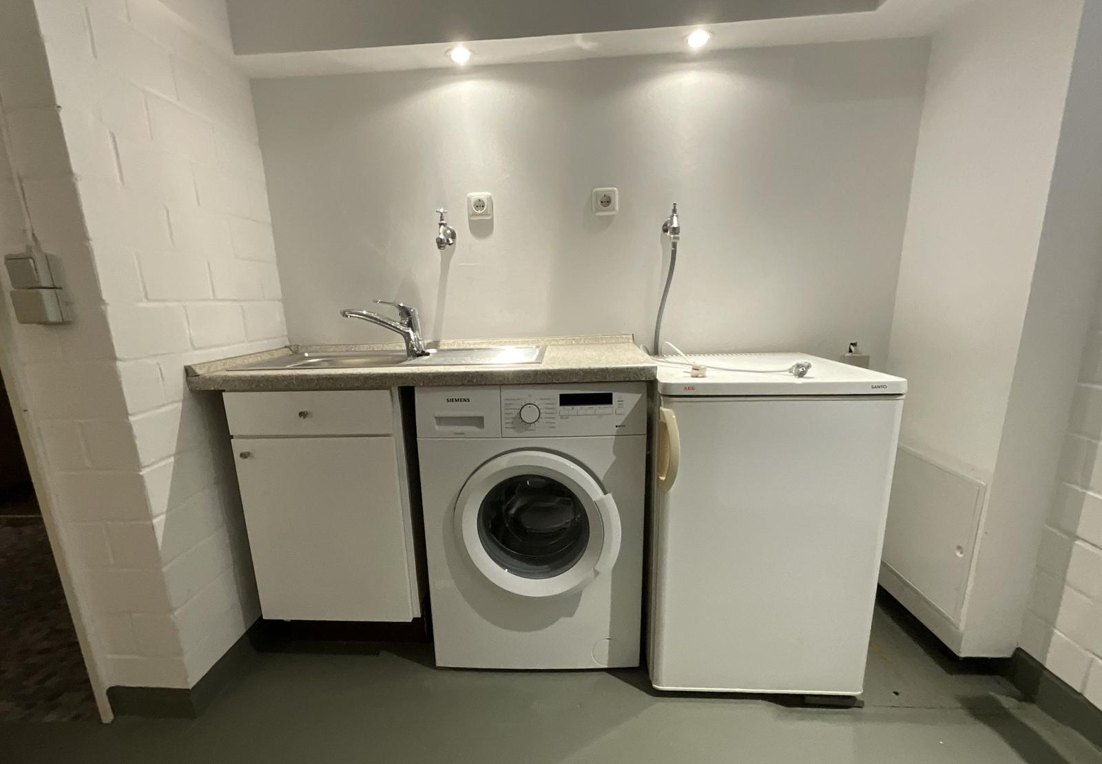 Wäscherei mit Waschmaschine, Spülbecken und Kühlschrank.