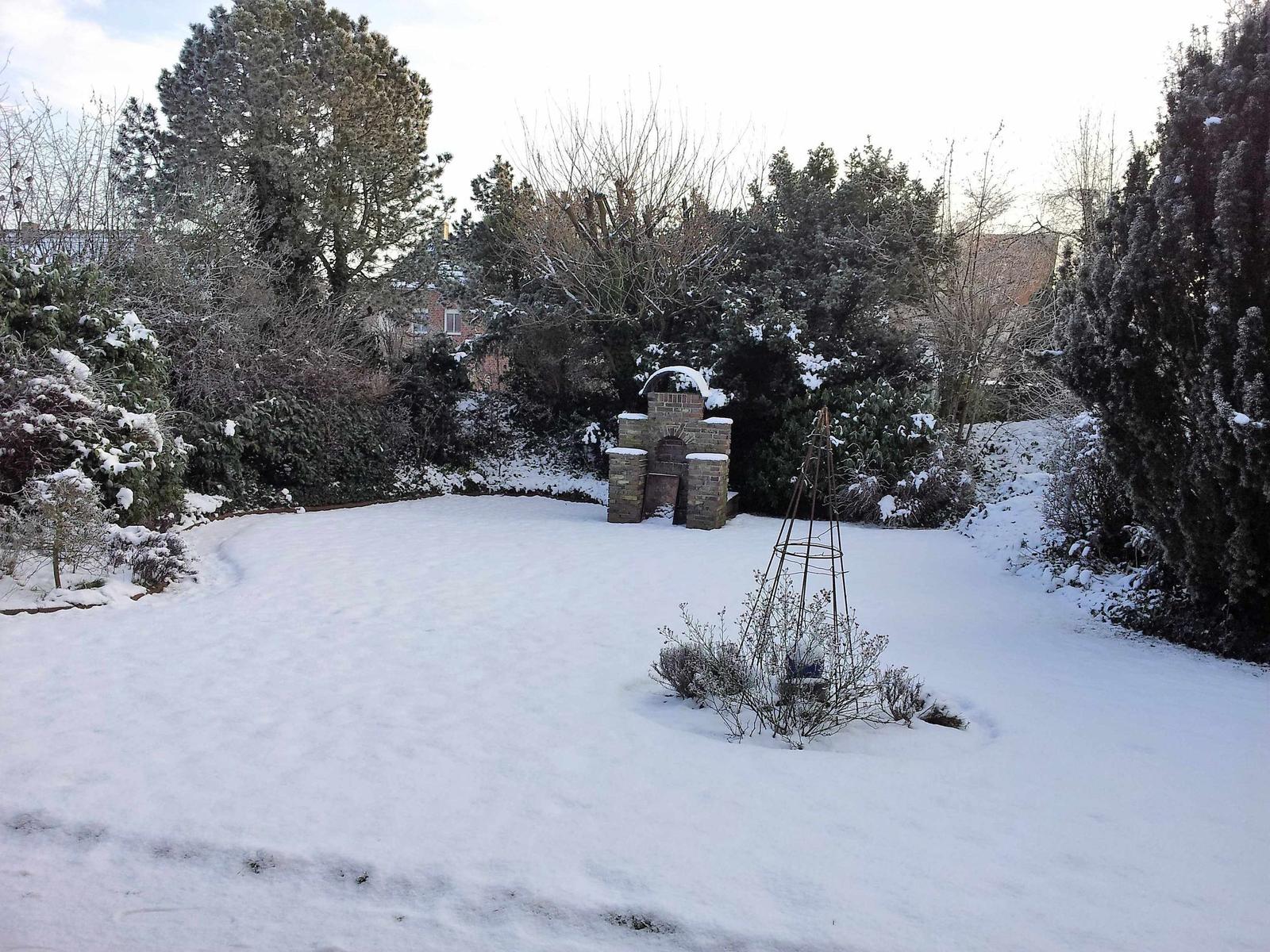 Schneebedeckter Garten mit Steinbau und Sträuchern.