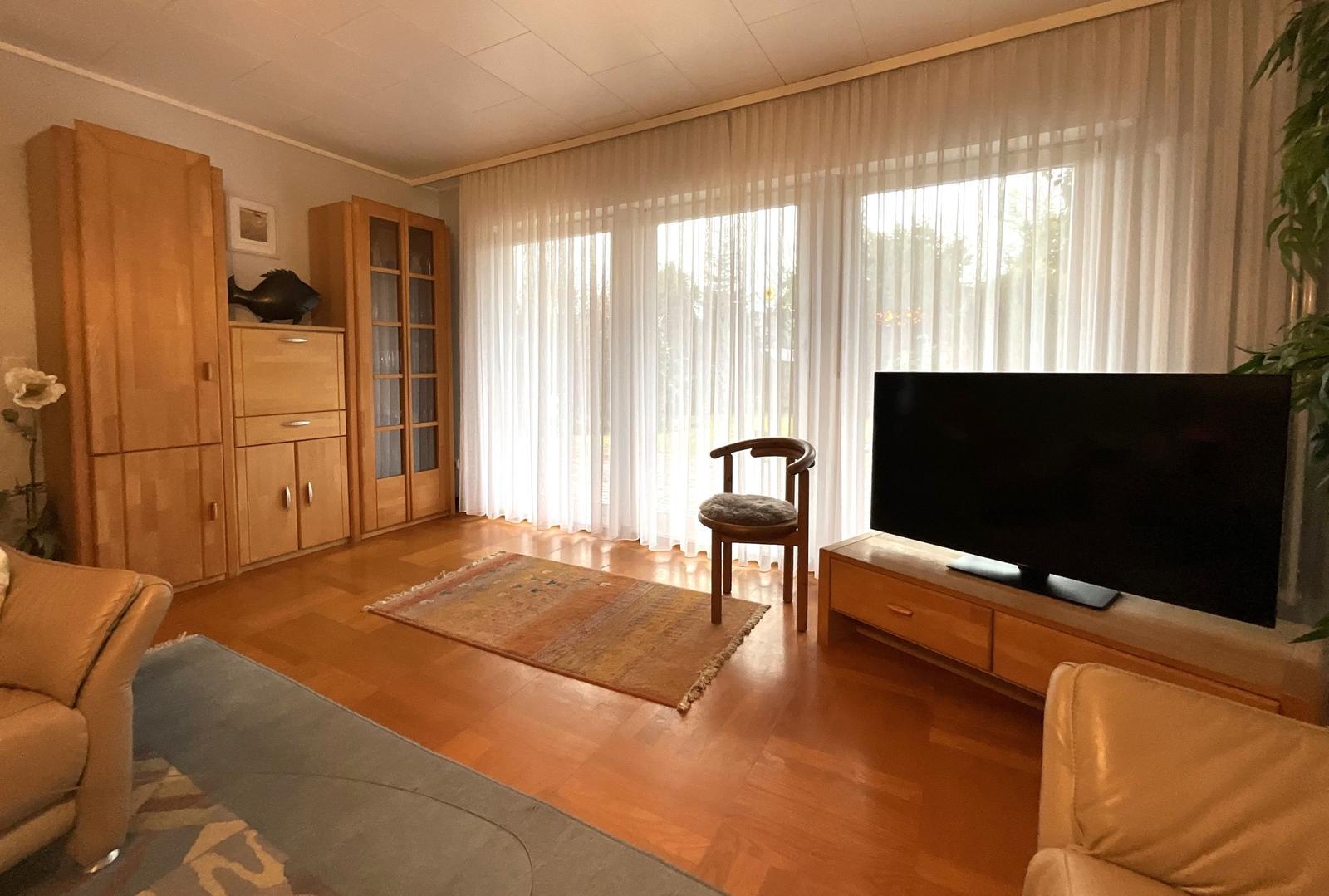 Wohnzimmer mit Holzmöbeln, Fernseher und großem Fenster