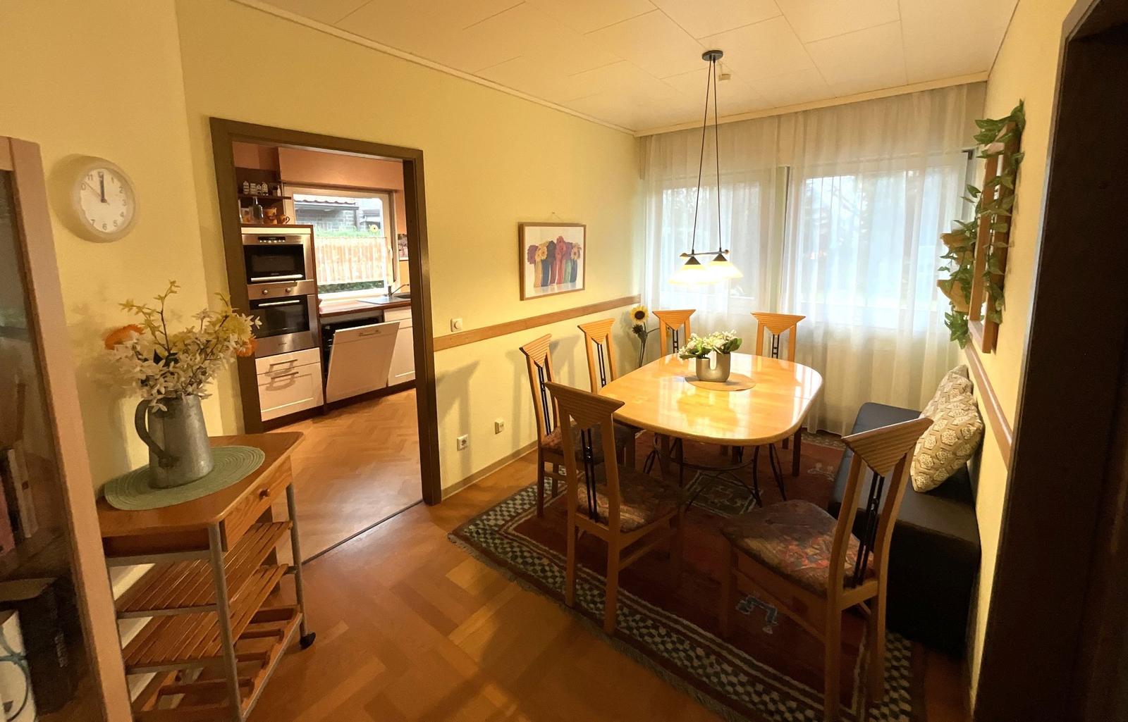 Esszimmer mit Holztisch, Stühlen und Blick in die Küche.