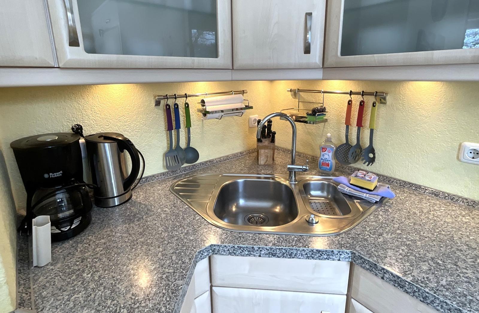 Küche mit Spüle, Kochutensilien und Kaffeemaschine auf Arbeitsfläche.