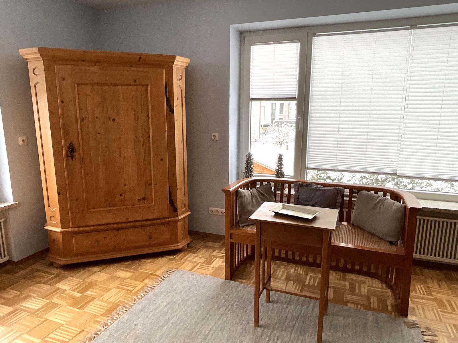 Ein Raum mit Holzschrank, Sitzbank und Tisch vor Fenster mit Jalousie.