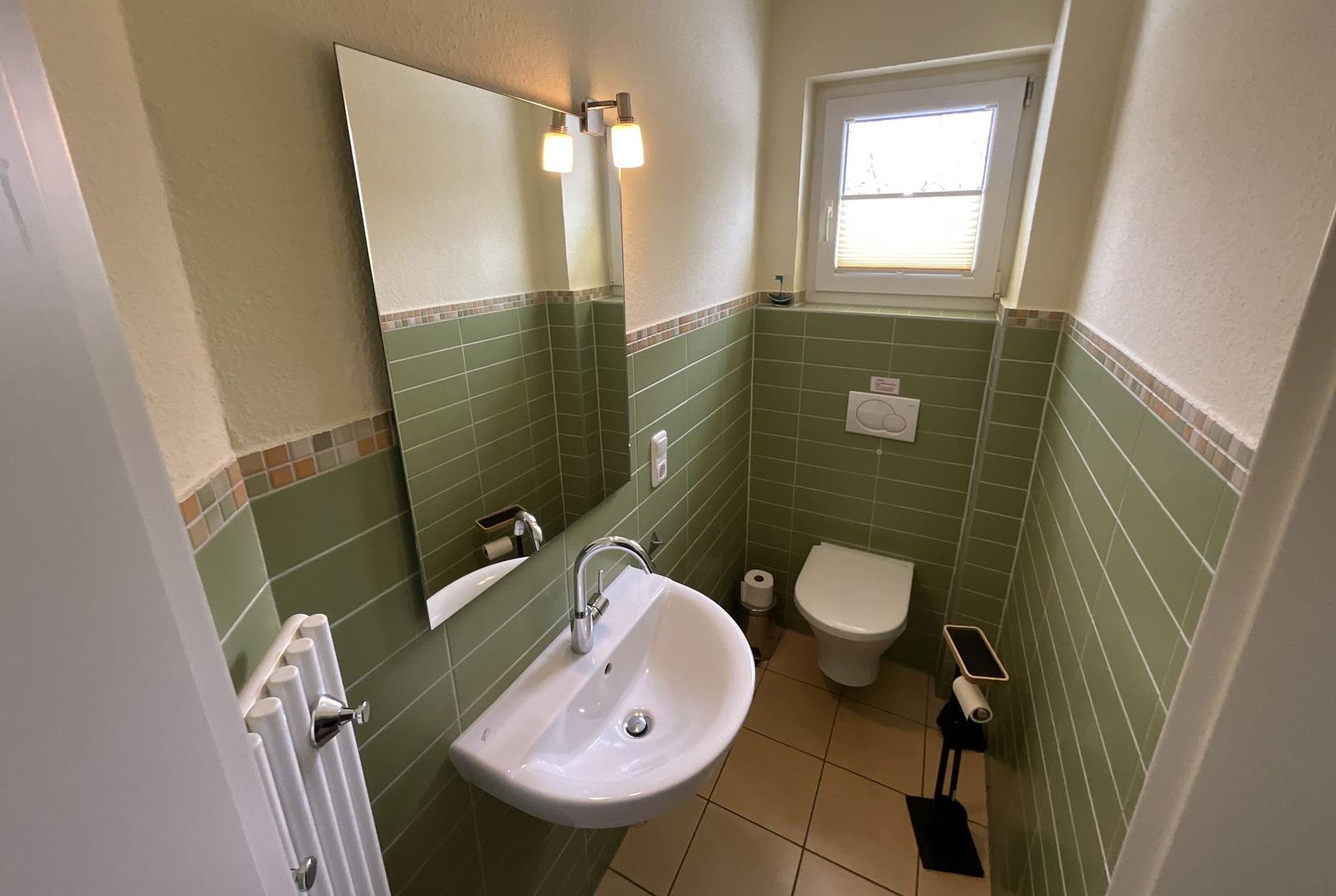 Badezimmer mit Waschbecken, Spiegel, Toilette und Fenster.