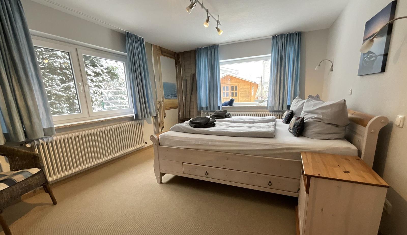 Schlafzimmer mit Doppelbett, Fenstern und Holzmöbeln.