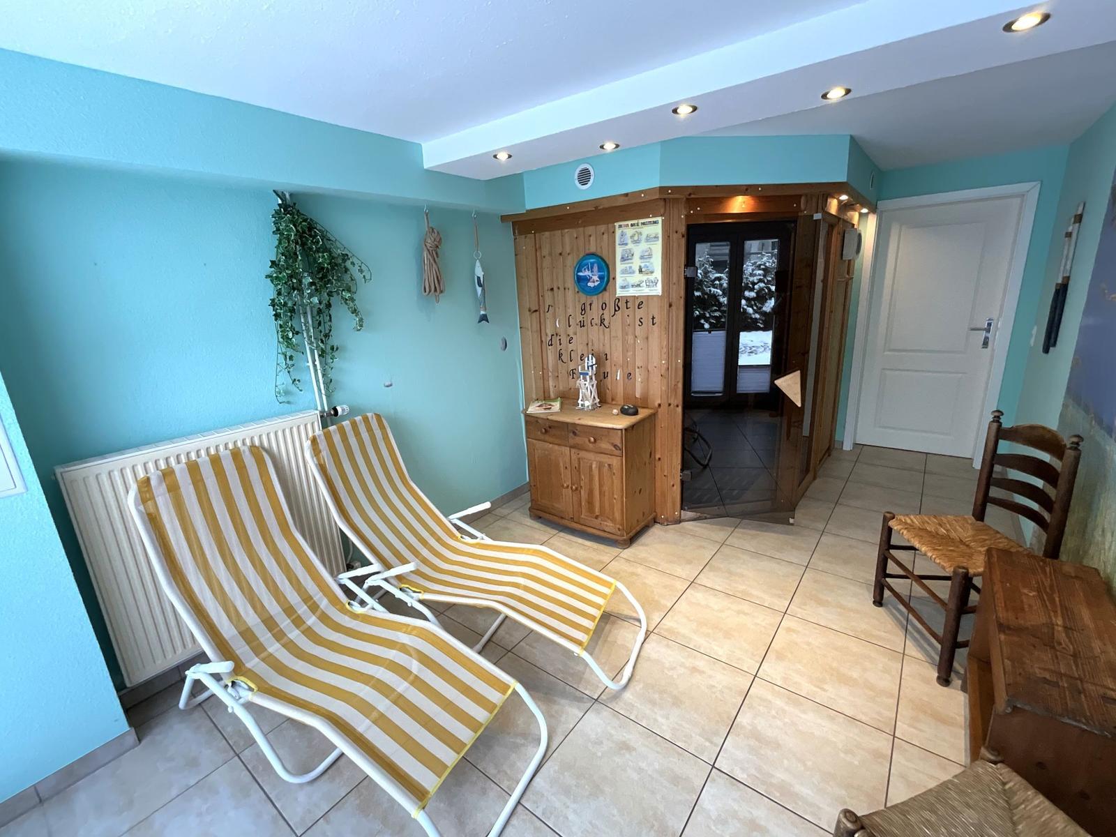 Zwei Liegestühle, Holzschrank und Tür in einem Raum mit hellblauen Wänden.