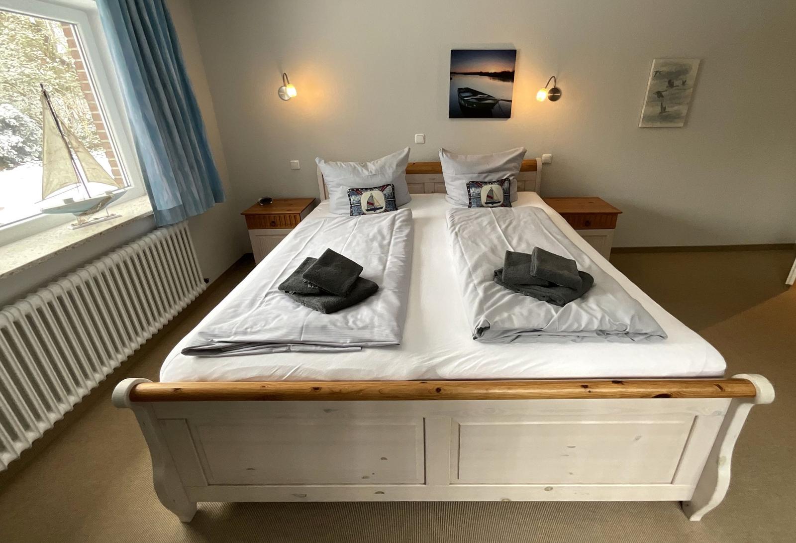 Schlafzimmer mit Doppelbett, zwei Nachttischen und Fenster mit Segelbootmodell.
