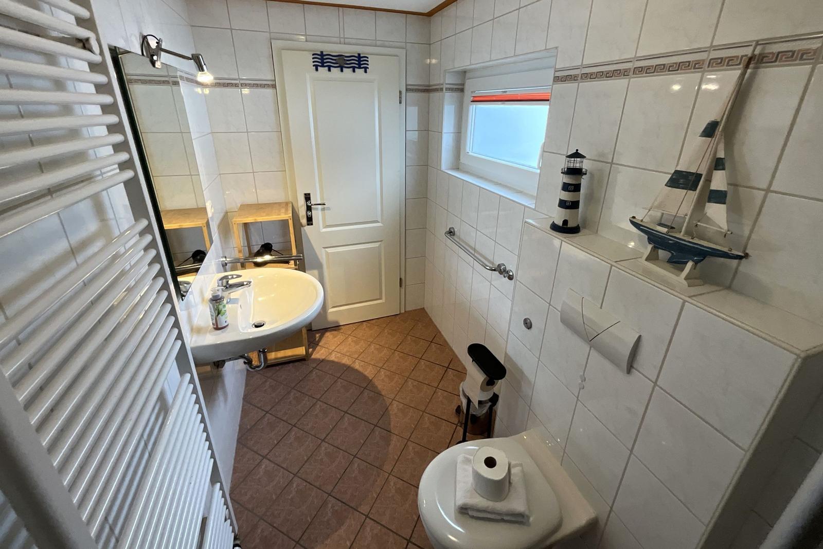Badezimmer mit Toilette, Waschbecken und Fenster. Dekoration: Leuchtturm und Segelschiffmodell.