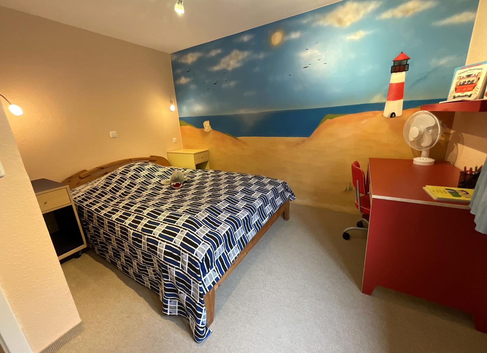 Schlafzimmer mit Strand-Malerei, Bett, Schreibtisch und Ventilator.