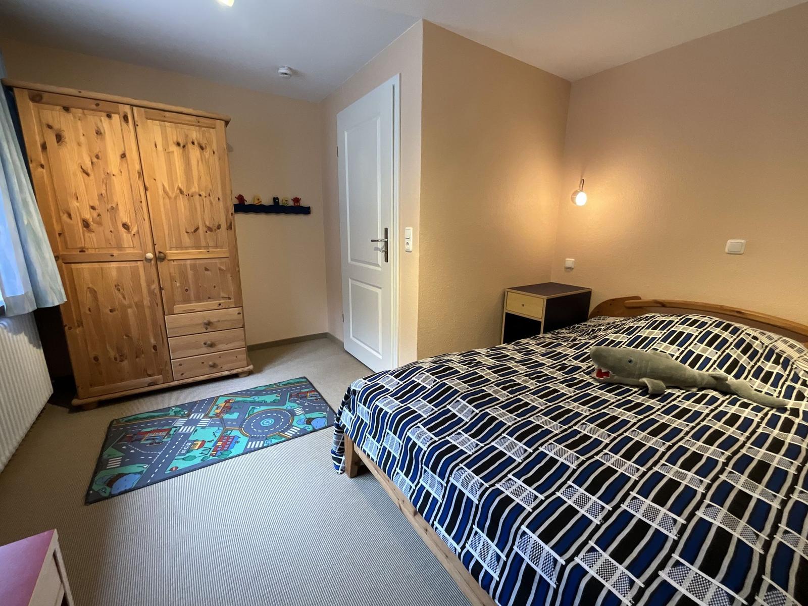 Schlafzimmer mit Bett, Kleiderschrank und Spielteppich.