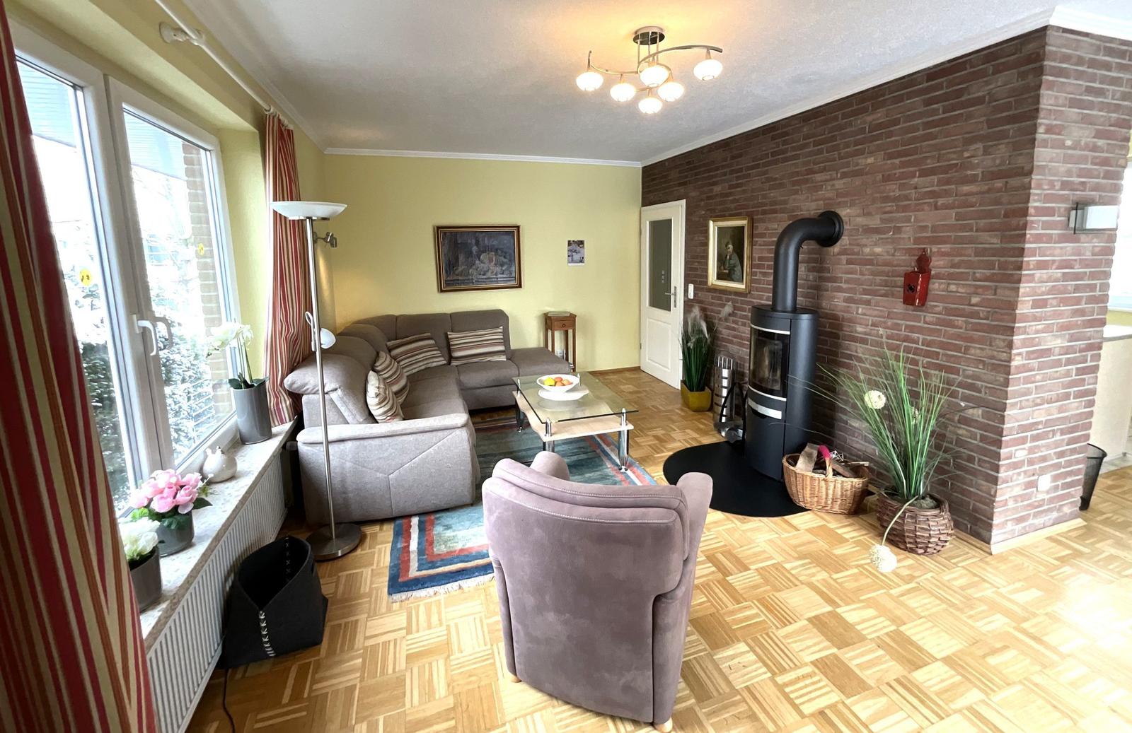 Wohnzimmer mit Sofa, Sessel, Kaminofen und Holzboden.