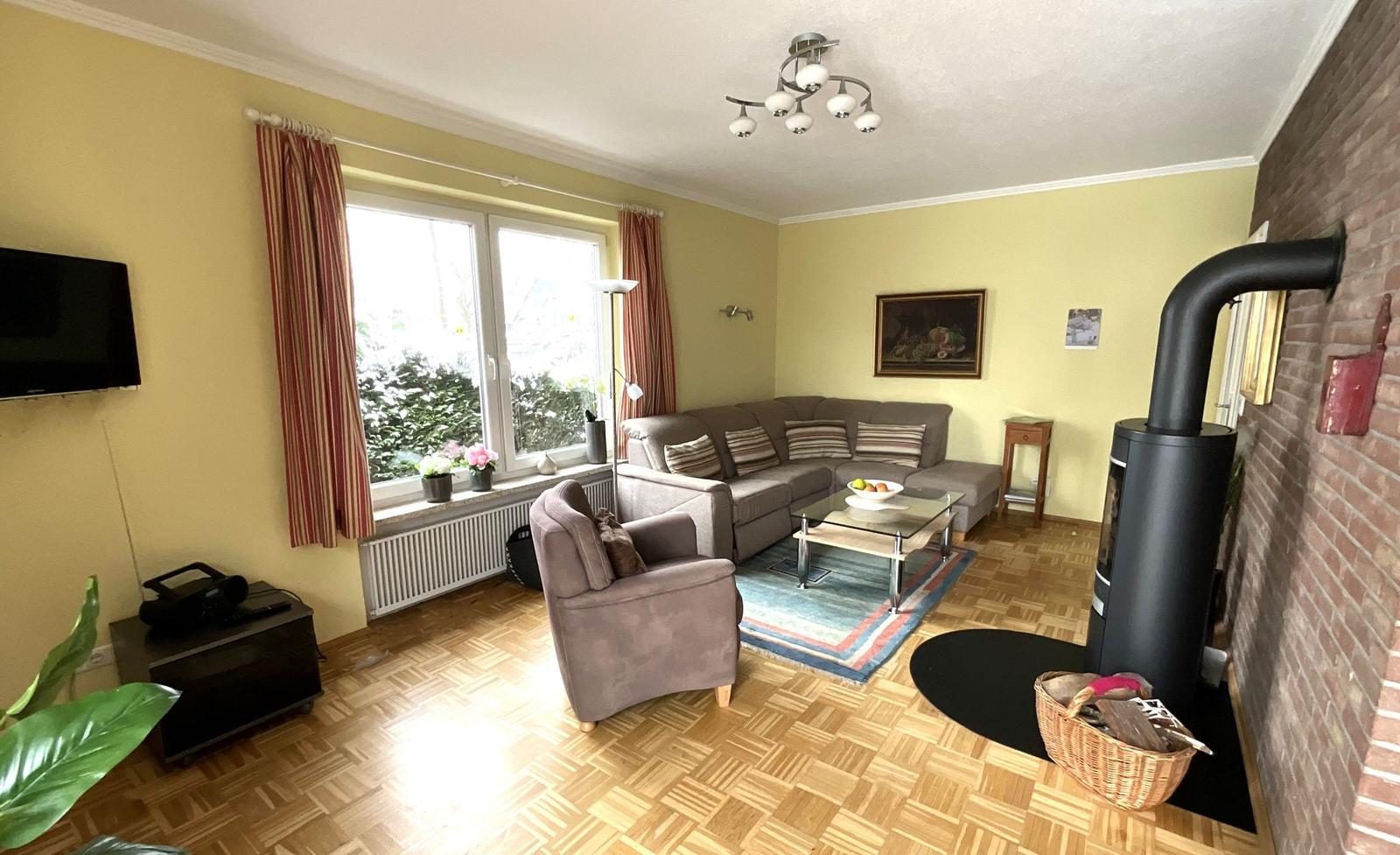 Wohnzimmer mit Sofa, Sessel, Fernseher und Kaminofen.