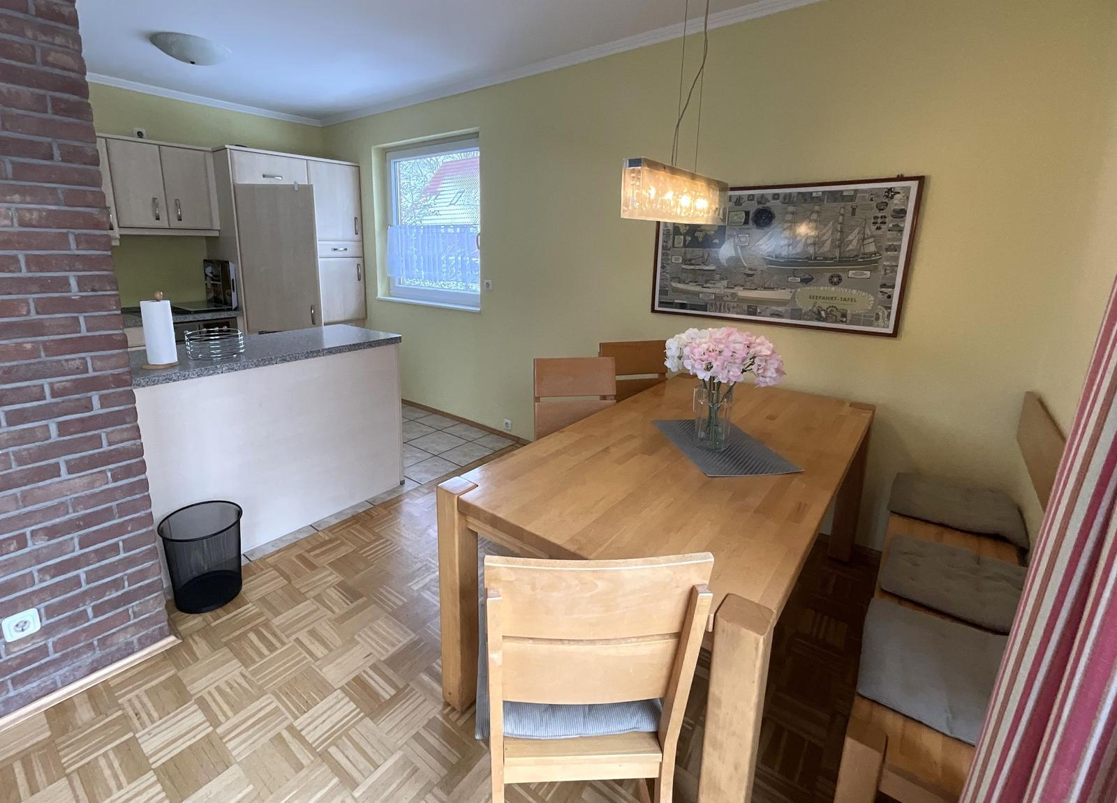 Essbereich mit Holztisch, Stühlen und Fenster. Küche mit Arbeitsplatte und Schränken.