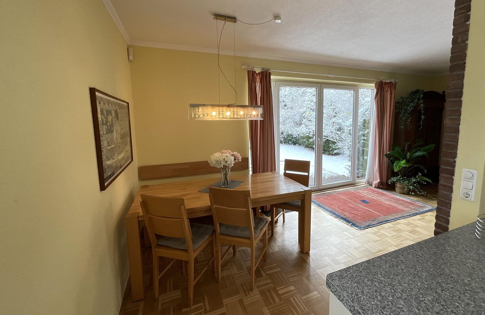 Esszimmer mit Holztisch, Stühlen und Blick auf Schnee. 