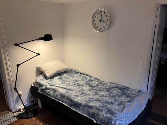 Ein Schlafzimmer mit einem Bett, einer Stehlampe und einer Wanduhr.