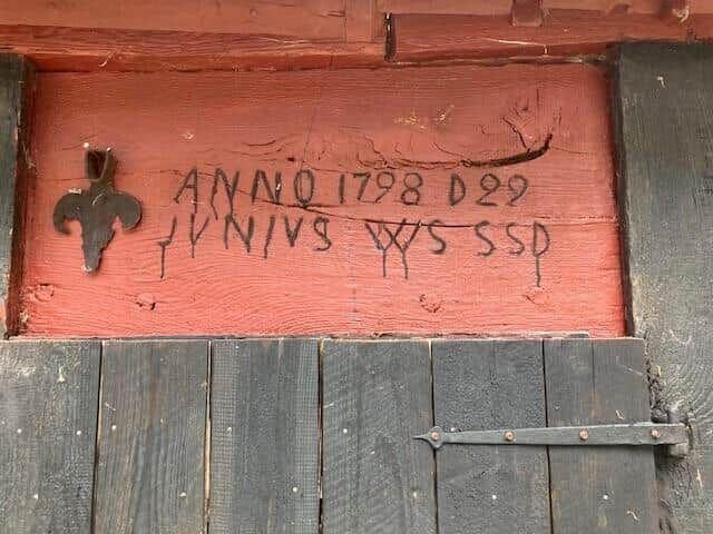 Holztor mit roter Tafel, auf der ANNO 1798 D29 und ein Kreuz eingraviert sind.