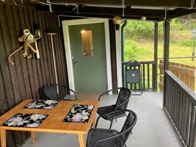 Terrasse mit Tisch, vier Stühlen und grüner Tür. Holzwand und Gartenblick.