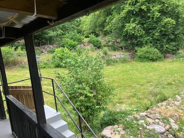 Vor dem Haus befindet sich ein grüner Garten mit Bäumen und einem Steigweg.