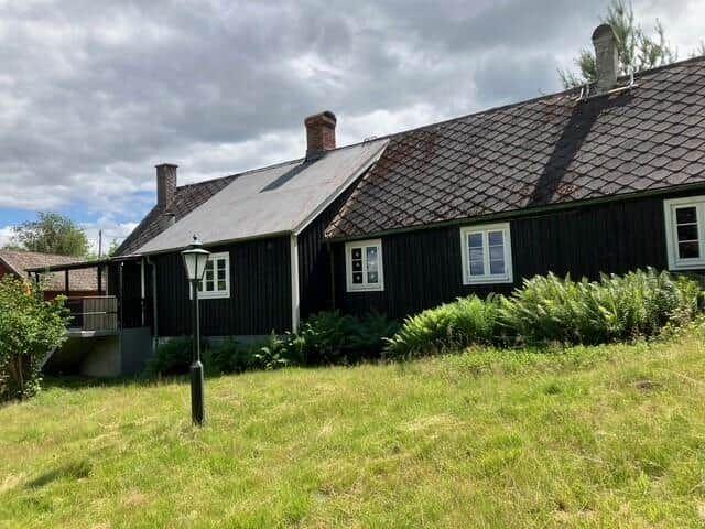 Schwarzes Holzhaus mit weißen Fenstern und Dachgauben im Grünen.