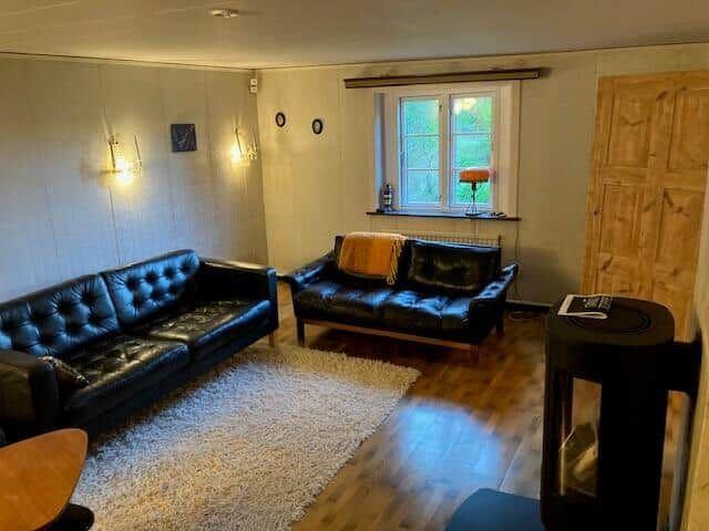 Wohnzimmer mit zwei Ledersofas, Holzboden und Fenster mit Blick auf Grün.
