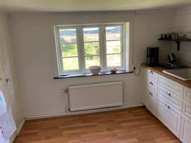 Küche mit weißer Einbauküche, Holzboden und Fenster mit Blick auf Landschaft.