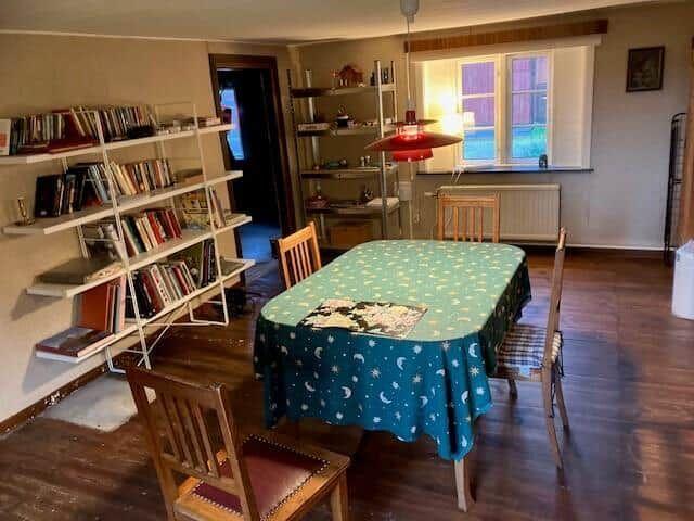 Esszimmer mit Tisch, Stühlen und Bücherregal an der Wand.