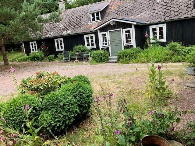 Schwarzes Holzhaus mit grüner Tür und Gartengrundstück.