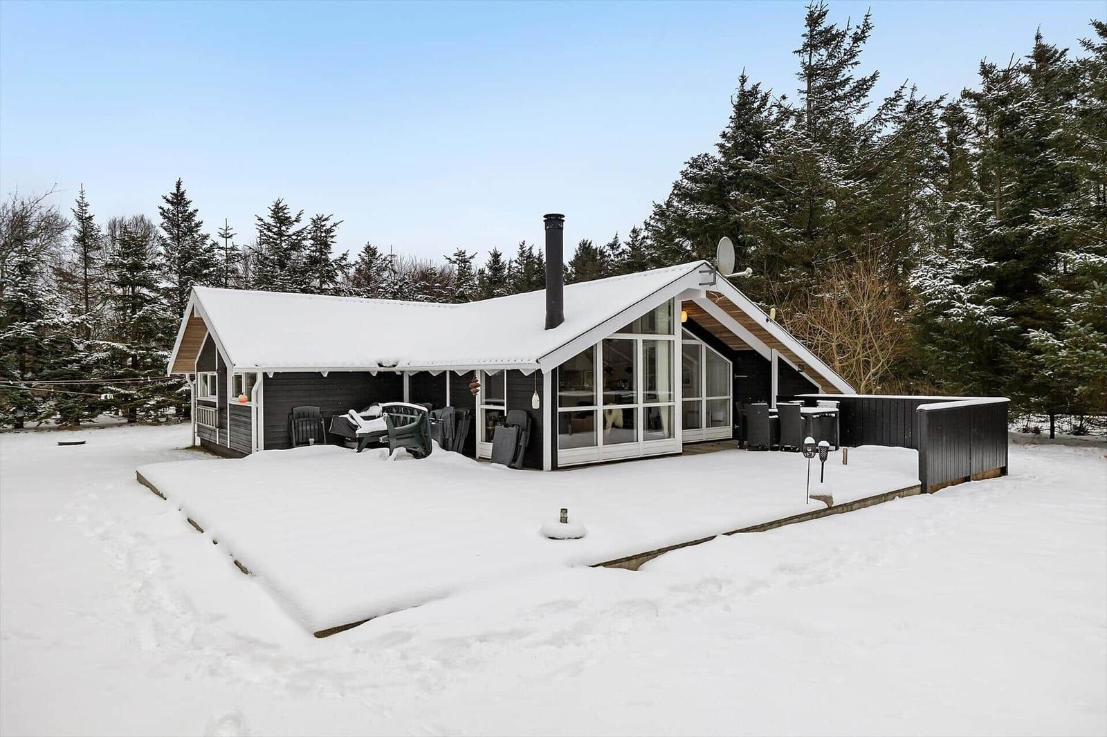 Snow-free terrace with seating area in front of modern wooden house.