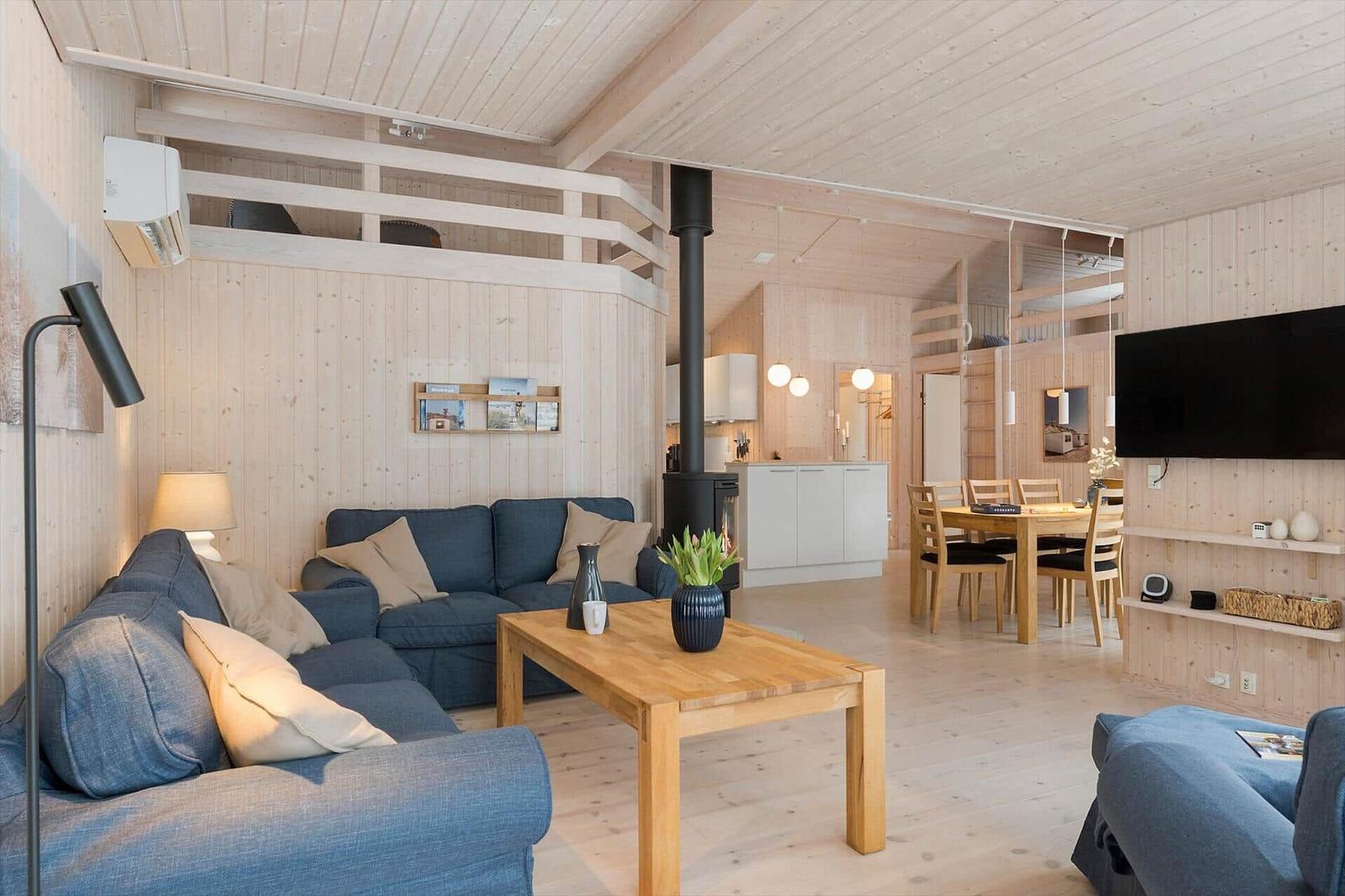 Living and dining area with wooden walls, sofa, dining table, and wood stove.