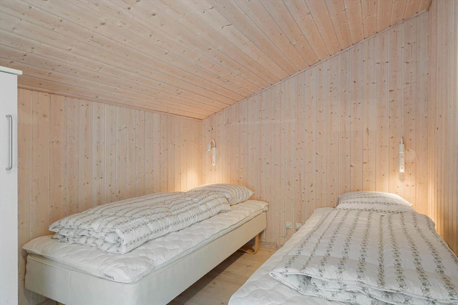 Two single beds in a room with wooden walls and wall lights.