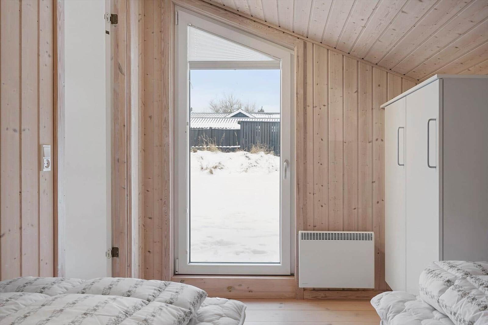Bedroom with wooden walls, window, and bed. Outside snow and fence.