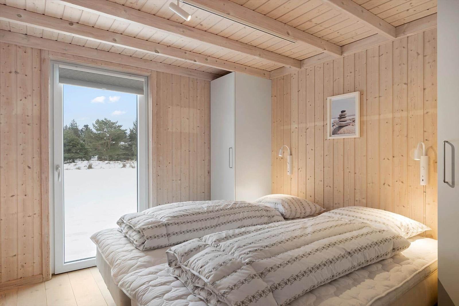 Bedroom with wooden walls and window view of snow and trees.